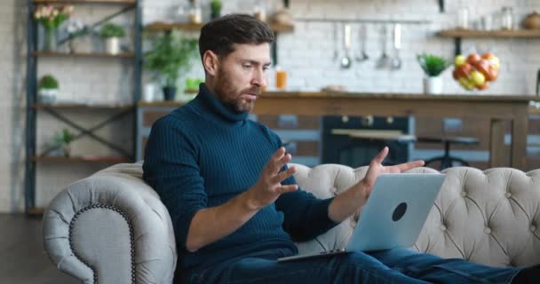 Vista laterale uomo barbuto imprenditore, parlando videochiamata, a casa seduto sul divano a casa. Formazione online, formazione a distanza, incontro d'affari, conferenza webinar. — Video Stock