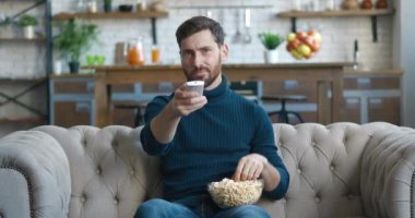 Genç sakallı adam evdeki kanepede oturuyor ve televizyon izliyor. Sıkıcı milenyum erkeği uzaktan kumandayı kullanarak ilginç video içeriği arar ve patlamış mısır yer.