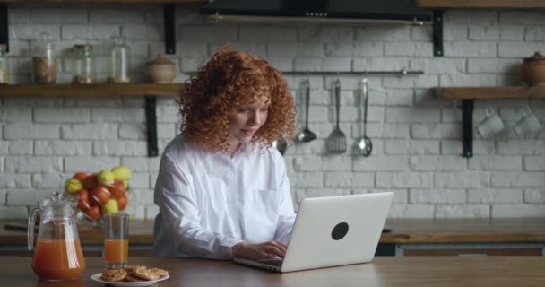 Opgewonden roodharige jonge zakenvrouw zit aan tafel met laptop computer werken in thuiskantoor keuken achtergrond. Ze krijgt geweldig nieuws en is blij. Ja gebaar laten zien — Stockvideo