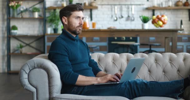 Pemuda berjanggut freelancer menggunakan perangkat laptop di sofa di kantor rumah, potret laki-laki bekerja jauh di komputer di apartemen — Stok Video