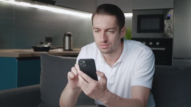 Ung mand bruger smartphone app, mens du sidder på sofaen derhjemme om natten. Teknologi, internet, kommunikation og menneskelige begreber – Stock-video