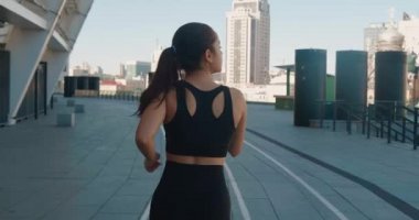 Ağır çekimde dışarıda koşan atletik genç bir kadının arka görüntüsü. Fitness kızı antrenman yapıyor, sabah şehir sokaklarında koşuyor.