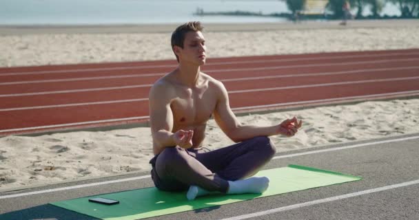 Jonge sportieve man zit in lotushouding mediterend buiten. Zen meditatie oefening, jonge atletische man mediteren buiten, zen gezondheid en welzijn — Stockvideo
