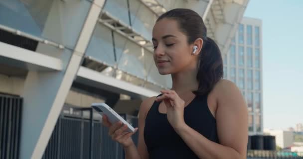 Adatta donna corridore utilizzando smartphone e ascoltare musica con auricolari dopo l'allenamento di fitness sportivo all'aperto vicino allo stadio — Video Stock