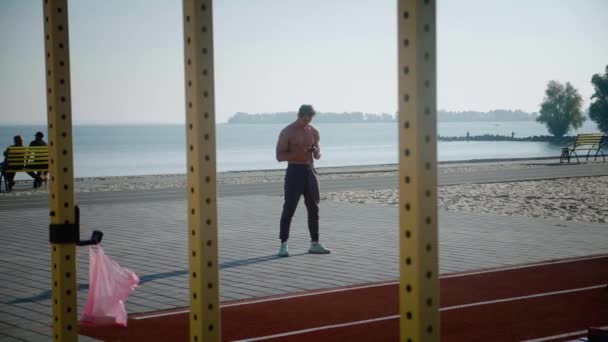 男子运动员在室外体育场锻炼期间使用智能手机 — 图库视频影像