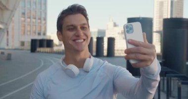 Genç yakışıklı fitness adamı stadyumda spor yaparken akıllı telefonuyla video görüşmesi yapıyor.
