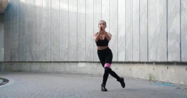 Güzel fitness genç kadın lastik bant direncini kullanarak sıkı sıkıya çömeliyor. Açık havada lastik elastik bantla kadın egzersizi.