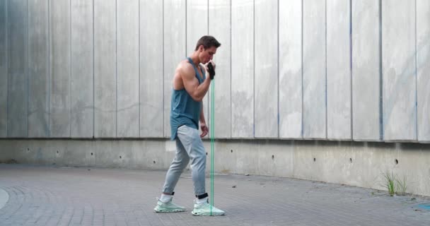 Jonge atletische man met behulp van een expander om te trainen biceps buiten. — Stockvideo