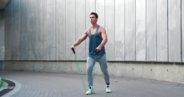 Jonge atletische man met behulp van een expander om zijn schouders buiten te trainen. — Stockvideo