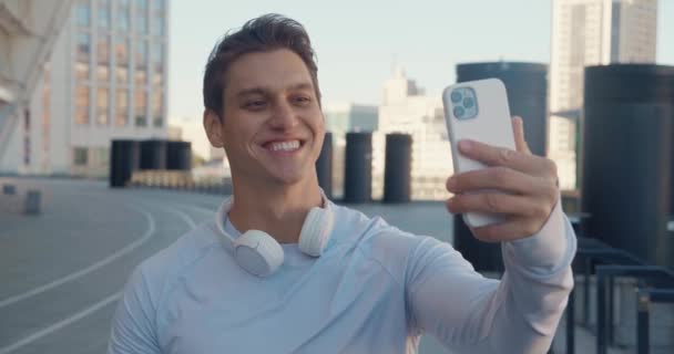 Joven hombre guapo de fitness que tiene videollamada con teléfono inteligente en la calle mientras el entrenamiento deportivo en el estadio — Vídeo de stock