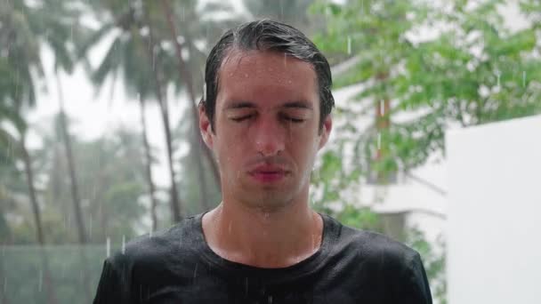 Portrait of pensive sad man standing in the pouring rain and getting soaked while looking into the sky. Slow motion shot — Stock Video