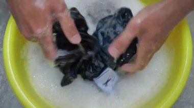 Erkek eli, banyo zeminindeki sarı leğende çamaşır yıkar. Ev rutini