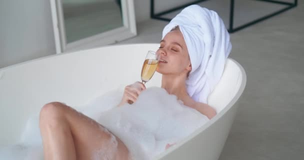Elbűvölő, örömteli nő hanyatlik a pezsgőfürdőben, élvezi a spa napot, fehér pezsgőt iszik. Szépség portré meztelen vonzó nő mosolyog ünneplő nap ki otthon fürdőszoba — Stock videók