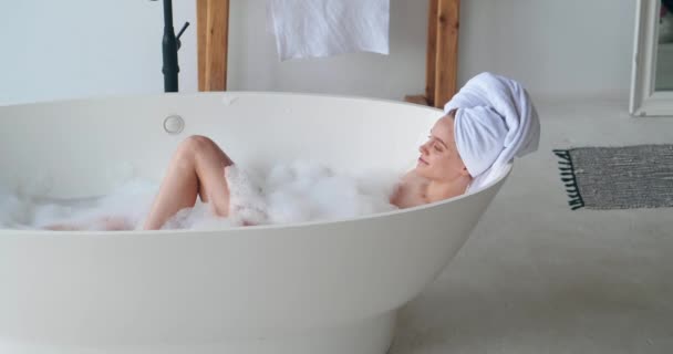 Aantrekkelijke vrolijke vrouw liggend in bad, genietend van een vrije dag thuis een bubbelbad nemen, spelen met schuim, glimlachen, tevreden kijken. Home spa, zuiverheid, reiniging, lichaam en huidverzorging concept — Stockvideo