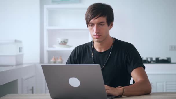 젊은 사업가 남성 프리랜서가 집의 식탁에 앉아 노트북으로 일하고 있습니다. 가정 직장. 가정 사무실. — 비디오