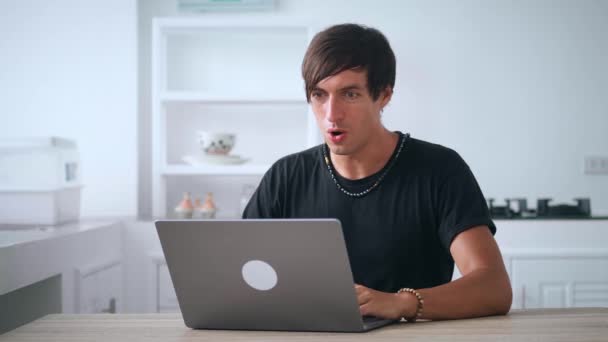 Emocionado hombre freelancer mirando portátil celebrar el éxito ganar apuesta en línea. Hombre joven afortunado leyendo grandes noticias y haciendo sí gesto mientras trabaja en la computadora en la cocina casera — Vídeos de Stock