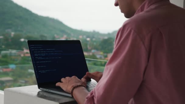 Rear view of programmer developer programmer freelancer writes code at a laptop outside the office on background of tropical jungle — Vídeo de stock