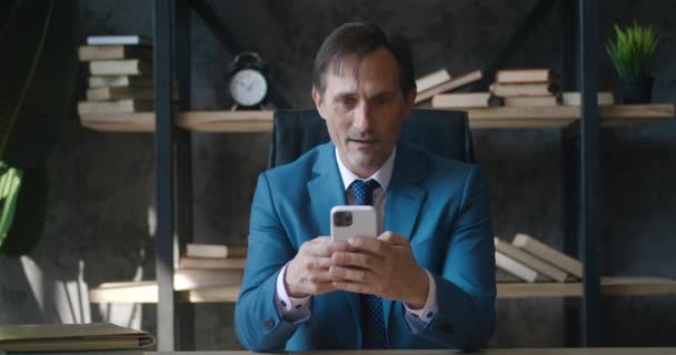 Happy senior business man receiving message offer opportunity, mature business man reading good news in smartphone, sitting at office. Excited overjoyed male looking at mobile phone show wow emotion — Vídeo de stock