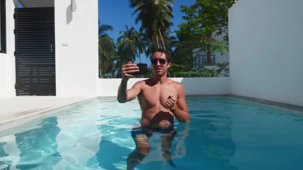 Young man holding mobile phone and video calling while holidays at hot summer day outdoors at luxury pool villa. — Vídeos de Stock