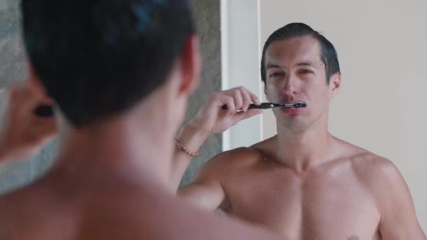 Anak muda menggosok giginya sambil berdiri di kamar mandi di depan cermin, rutinitas pagi — Stok Video