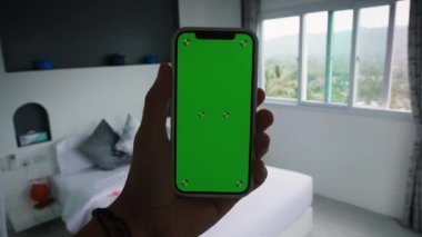 Yatak odasında ya da otel odasında Yeşil Model Ekran Krom Anahtarı olan Mans Hand Holding Smartphone. Yüksek kalite 4k görüntü