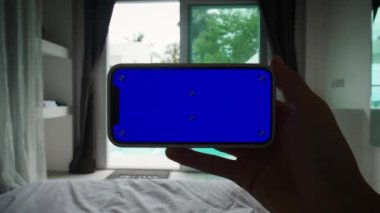 Yatak odasında ya da otel odasında Yeşil Model Ekran Krom Anahtarı olan Mans Hand Holding Smartphone. Yüksek kalite 4k görüntü