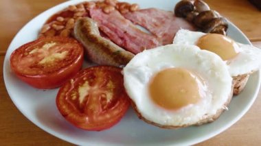 Top view of a traditional English breakfast in a plate on a wooden table. Eggs benedict, bacon, beans and tomatoes with bread ready to eat in a cafe. High quality 4k footage