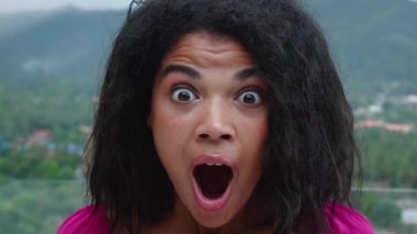 Close-up portrait of a young multiethnic woman looking at camera, rejoicing, expressing stupefaction and astonishment