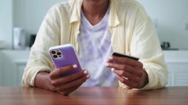 Detail: hands holding credit or discount card, transfering the data into a smartphone, making online payments from home