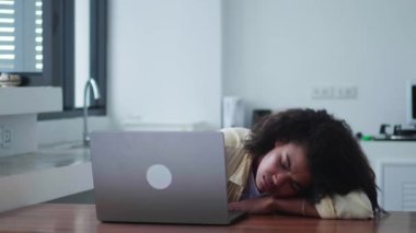 Young overworked woman closing the laptop cover and trying to relax, leaning her head on a table in home interior