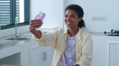 Charming young woman is talking by video link at a light home kitchen interior. Online communication concept