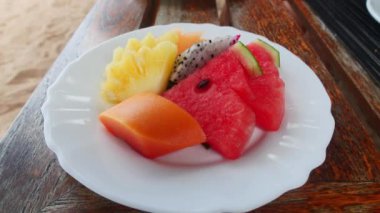 Exotic fruit slices of pineapple, dragon fruit, yellow mango, watermelon, served on a white plate in a restaurant menu.