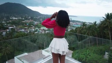 Steadicam shot of African woman on balcony, enjoying an amazing view of tropical Asian nature on rainy and overcast day