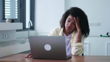 Bored woman has difficulties for achieving work and fixing problems, looking aside, with despair while working on laptop
