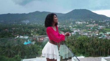 Smiling beautiful African woman on a balcony with amazing views of tropical nature and seaside on a foggy and rainy day