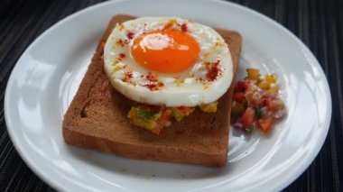 Rotating shot of a toasted whole grain bread with raw vegetables and roasted egg on a white plate in a restaurant menu.