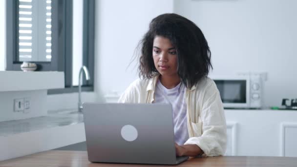 リモートワークやオンライン学習のためのラップトップコンピュータを使用して若い女性をマルチタスク 自宅のインテリアでキッチンテーブルで — ストック動画
