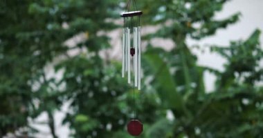 Rüzgar Çanları evin verandasında yeşil ağaçların arka planında asılı duruyor. 4K