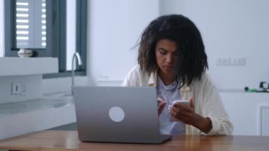 Çoklu görev yapan kadın telefonunu kontrol ediyor ve uzaktan çalışırken bilgisayarına veri aktarıyor. Çevrimiçi ödemeler