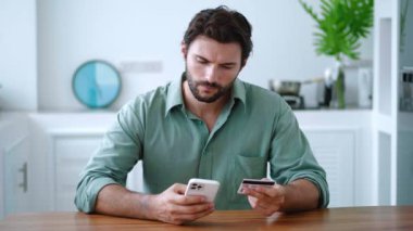 Çekici beyaz adam online ödeme yapıyor, elinde akıllı telefon kullanarak banka kartı tutuyor. Finans, internet alışverişi.