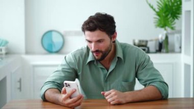 Hispanik adam akıllı telefon kullanarak haberleri kontrol ediyor, sosyal medya içeriğine göz atıyor, internette sohbet ediyor, heyecanını dile getiriyor.