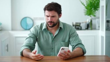 Sinirli ve sinirli, koyu renk saçlı genç bir adam. Uygulama veya telefonun şarjı bittiği için kızgınlığını dile getiriyor.