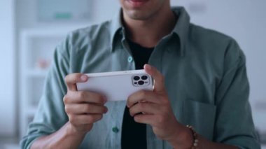 Akıllı telefondan yarış oyunu oynayan genç bir adam, bir ev evinin arka planına karşı mobil oyunlarda kazanılan mutlu zaferi kutluyor. Yüksek kalite 4k görüntü