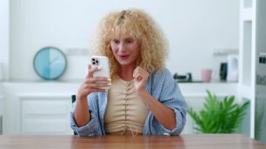 Gündelik giysiler içinde güzel bir kızıl kadın, modern akıllı telefonunu kullanıyor, internette sohbet ediyor, tatlı dişli bir gülümseme takınıyor.