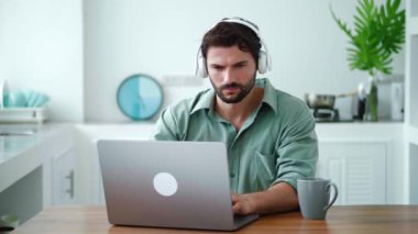 Ses kulaklıklı çekici genç adam, rahat hissediyor, evden bilgisayarla uzaktan çalışırken müzik dinliyor.