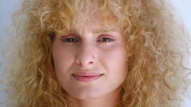 Kıvırcık saçlı, taze ve parlak tenli genç bir kadın kameraya tatlı tatlı bakıyor. Güzel, çeşitli insanlar.