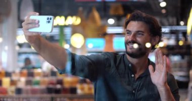 Yakışıklı sakallı adam uzanmış elleriyle akıllı telefonu tutuyor, güzel dişli bir gülümsemeyle video görüşmesi yapıyor..