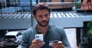 Plastik kart ve akıllı telefon kullanan çekici beyaz bir adam parayı banka hesabına başarıyla aktarıyor.