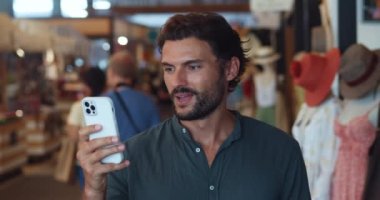 Telefon kullanan haylaz bir adam, erkek giyim mağazasından alışveriş yaparken tasarruf yapmak için internet sitelerinden alışveriş yapıyor.