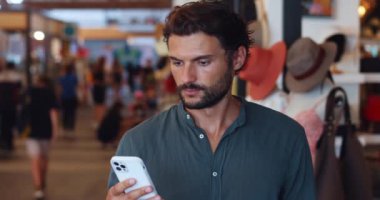 Akıllı telefon kullanan yakışıklı bir adam, yeni moda kıyafetler ve moda aksesuarlar ararken alışveriş merkezinde duruyor.